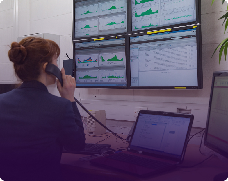 specialist on the phone monitoring real-time performance graphs on multiple wall-mounted displays