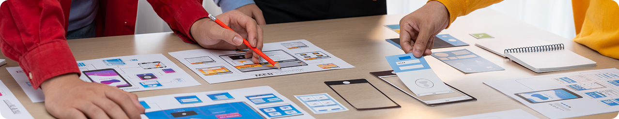 Team members collaborating over app wireframes, UI paper mockups, and layout sketches during a software audit process