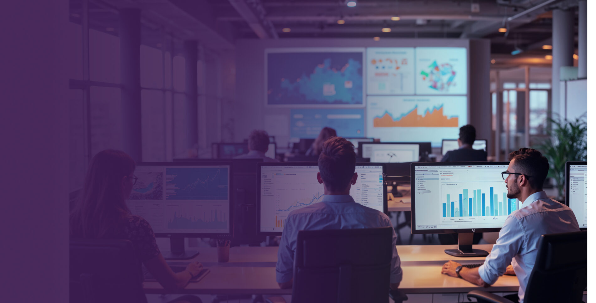 Two software developers sitting at desks in a dark office, viewing data charts and metrics on desktop monitors.