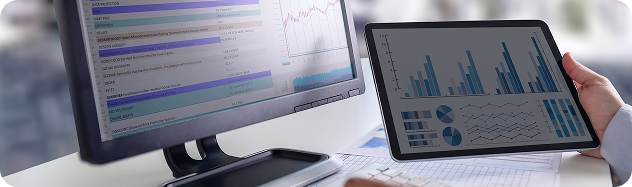 Financial analyst holding a tablet displaying data charts next to a desktop computer showing budget analytics